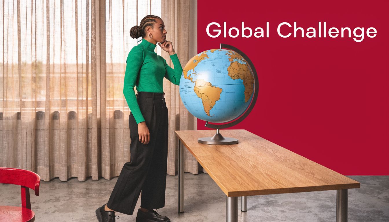 A professional woman standing by a desk looking thoughtfully at a large globe in a modern office.