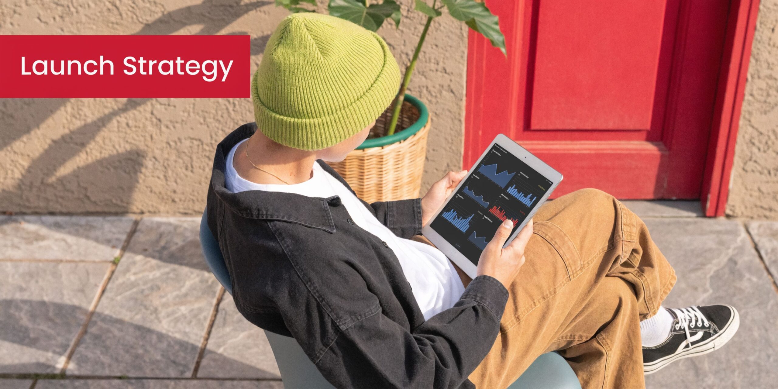 A person wearing a lime green beanie looking at financial charts on a tablet outdoors.