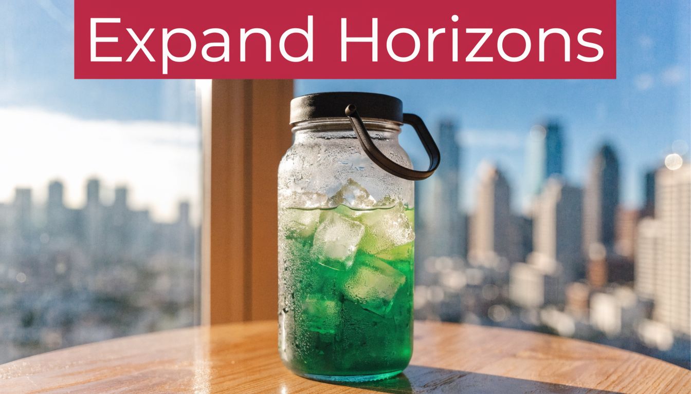 A glass jar filled with green liquid and ice cubes sits on a table overlooking a city.