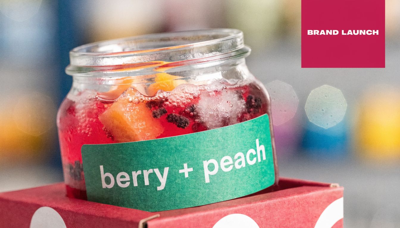 A glass jar filled with red berry and peach drink sitting on a red polka dot box.
