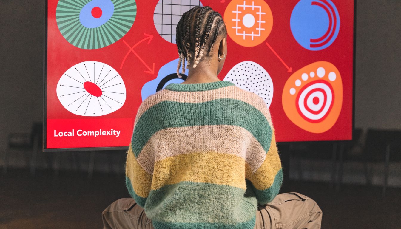 A person sitting in front of a screen displaying abstract graphic designs related to local complexity concepts.
