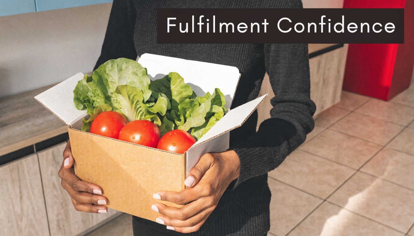 A person holding a cardboard delivery box filled with fresh lettuce and ripe red tomatoes.