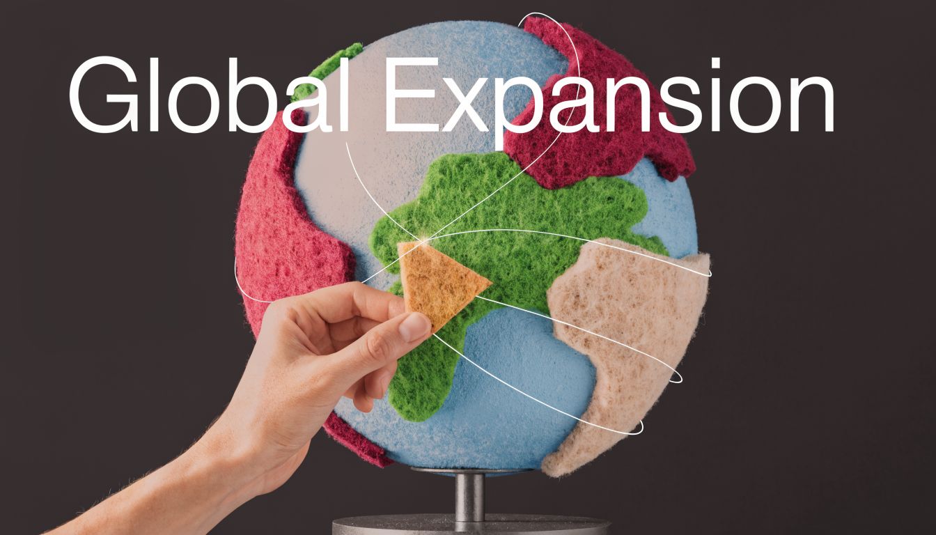 A hand placing a textured piece onto a felt globe representing global expansion and interconnected business strategy.