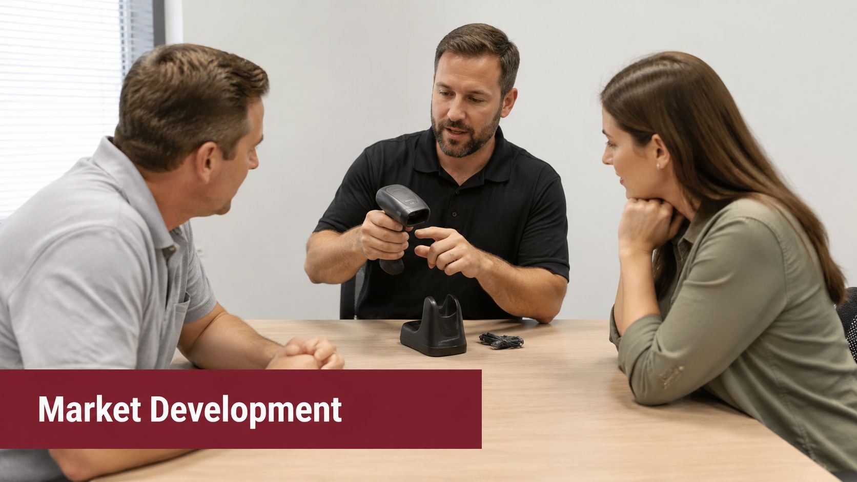 A professional business meeting discussing equipment with a barcode scanner on a table between three colleagues.